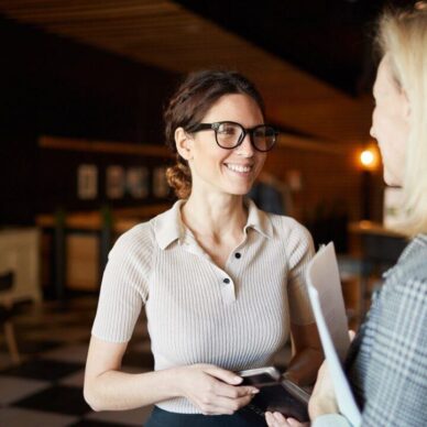 Two young successful businesswomen in smart casual having discussion of business plans for the next day in dark restaurant after work