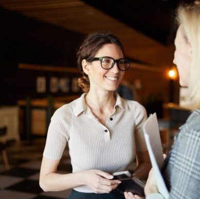 Two young successful businesswomen in smart casual having discussion of business plans for the next day in dark restaurant after work